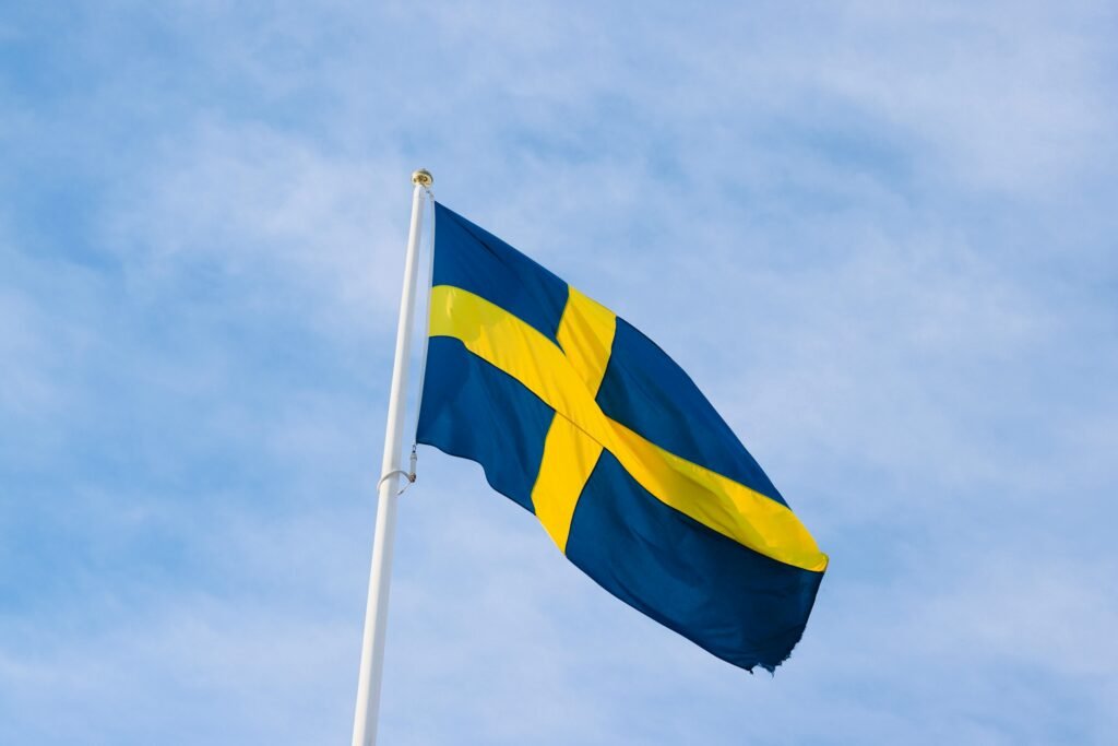 A vibrant Swedish flag on a flagpole against a clear blue sky in Jönköping, Sweden.